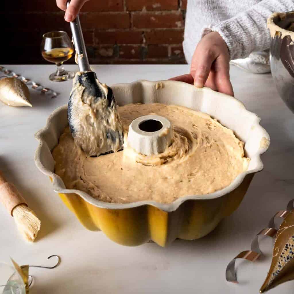 using a rubber spatula to smooth out the cake batter in the bundt pan