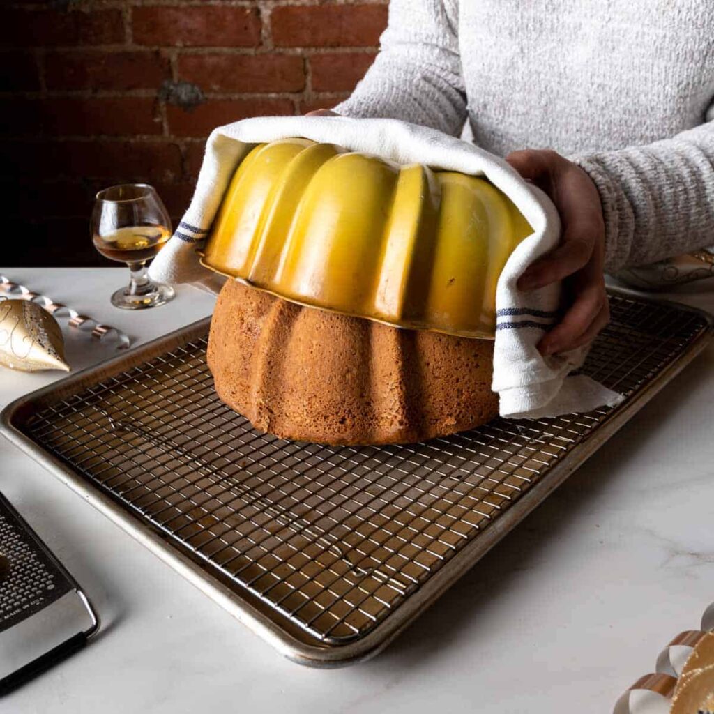 Using a kitchen towel to carefully remove the bundt pan from the freshly baked eggnog cake
