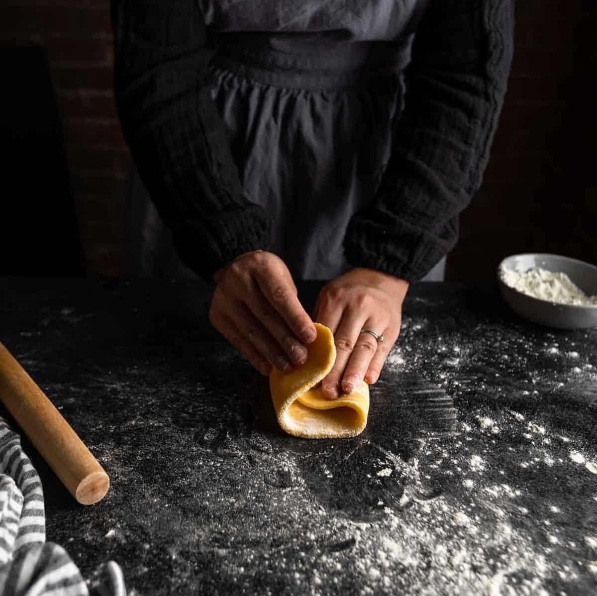 A woman folding an oval of pasta dough in thirds.