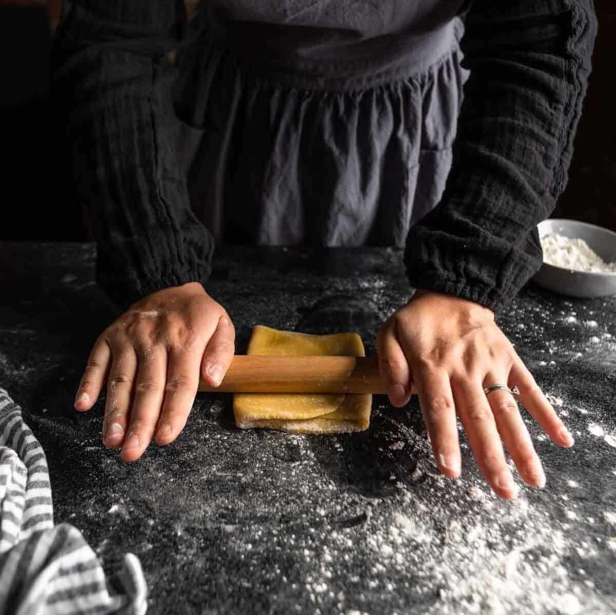 Rolling the folded pasta dough flat with a small rolling pin.