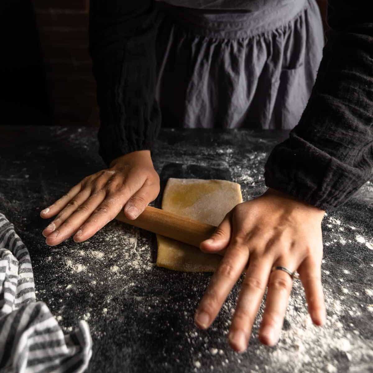 A woman rolling a piece of pasta dough into a long sheet.