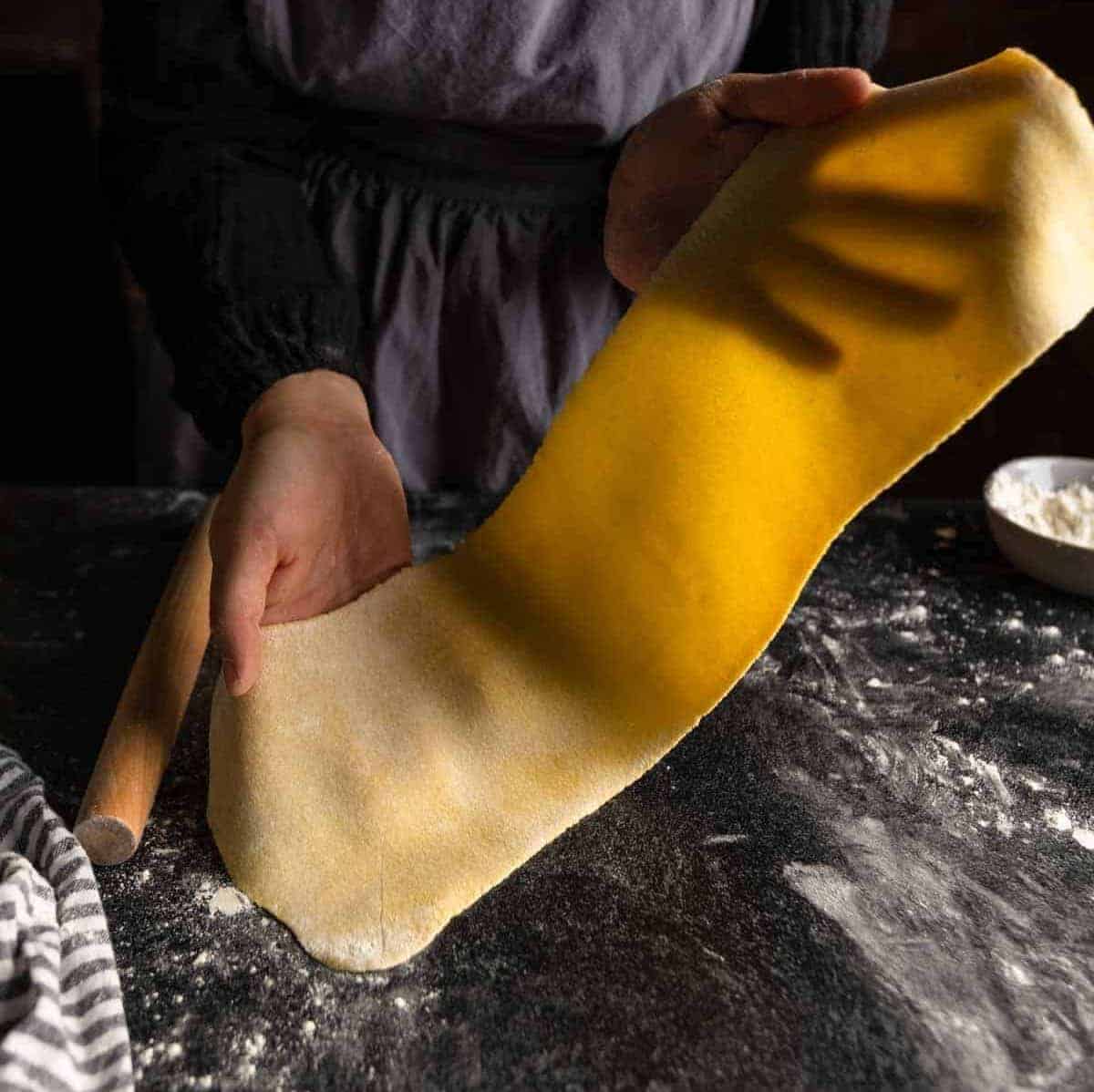 hands holding up a translucent sheet of semolina pasta dough