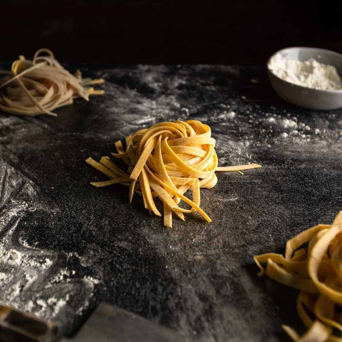 A nest of golden colored fettuccine noodles on a floured counter top.