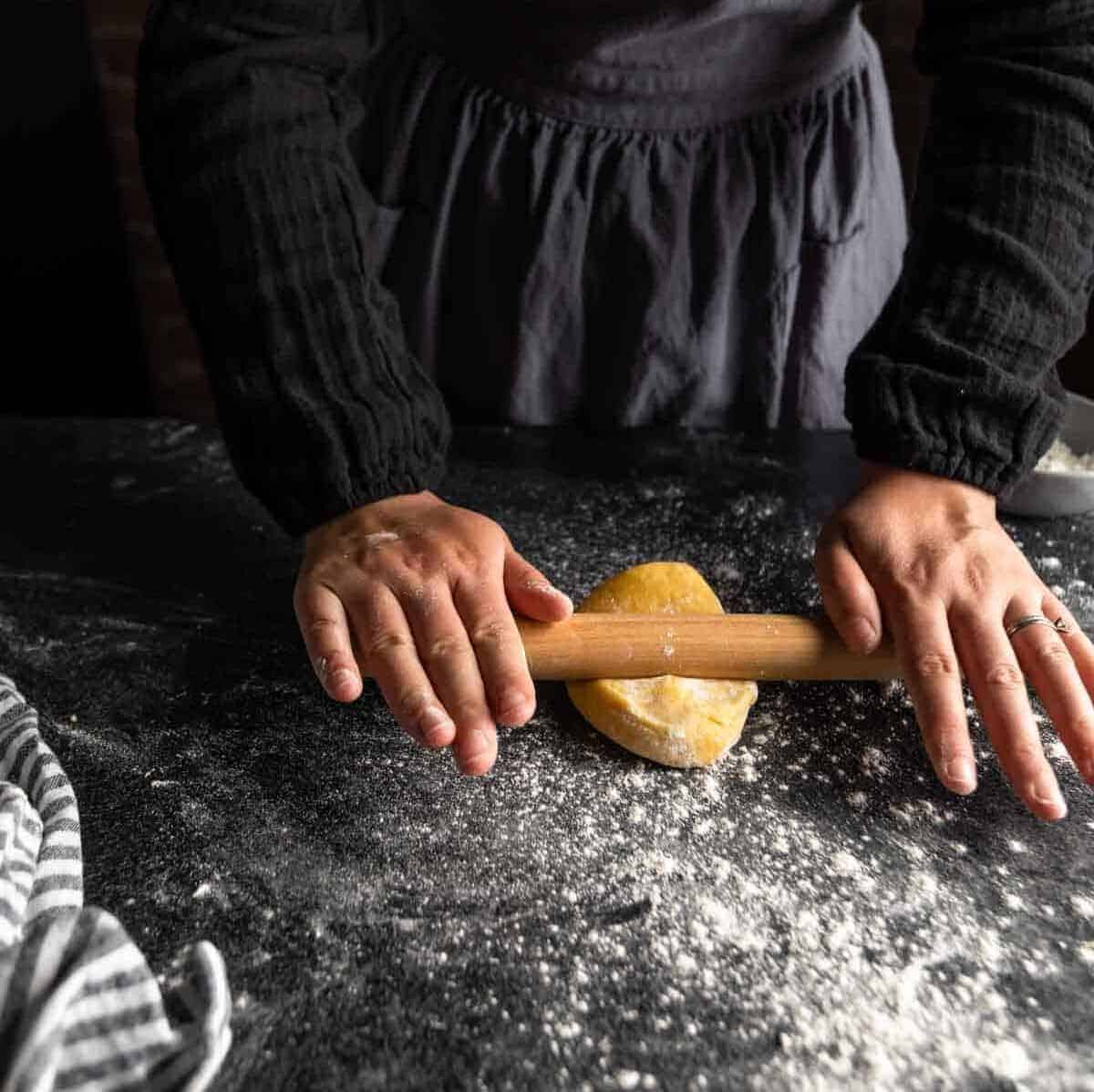 A woman rolling a small portion of semolina pasta dough.