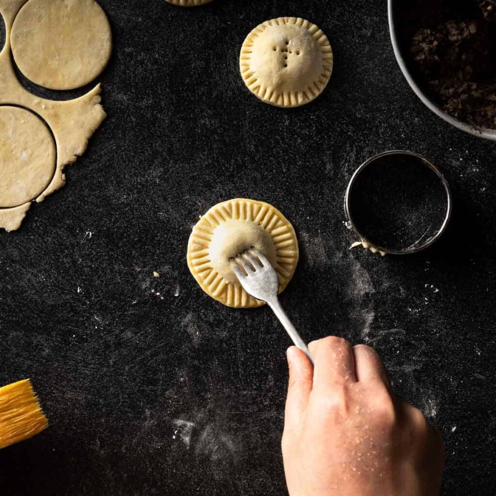 A fork poking holes in the top of a mini mushroom pie