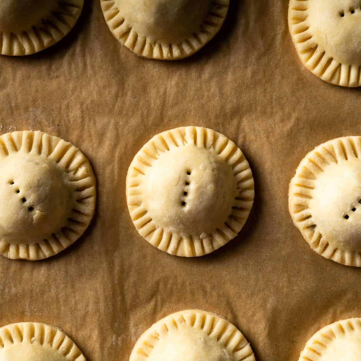 Rows of unbaked mushroom pies on a sheet of brown parchment paper