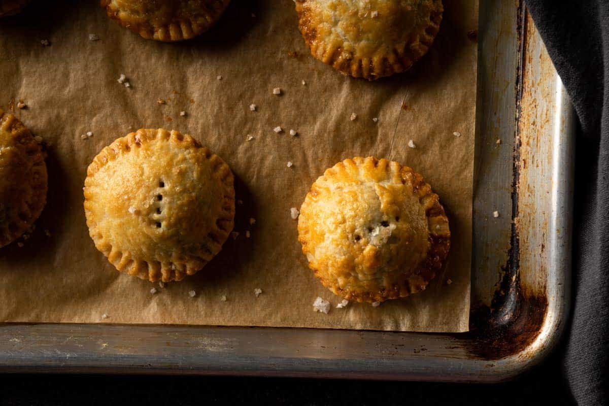 Golden brown baked mini mushroom pie surrounded by a sprinkle of flaky sea salt on a parchment lined baking sheet