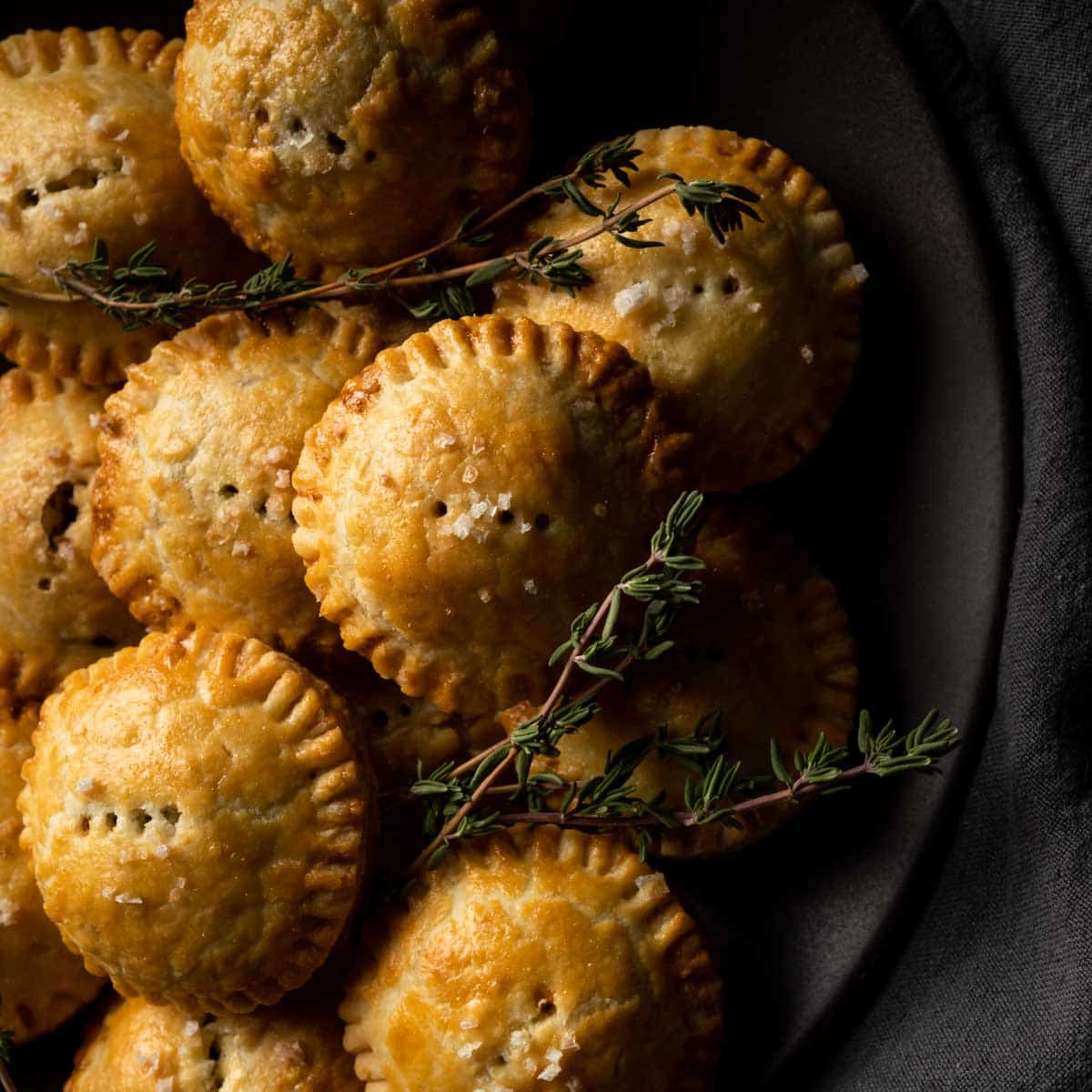 A plate stacked with mini mushroom pies and fresh thyme sprigs