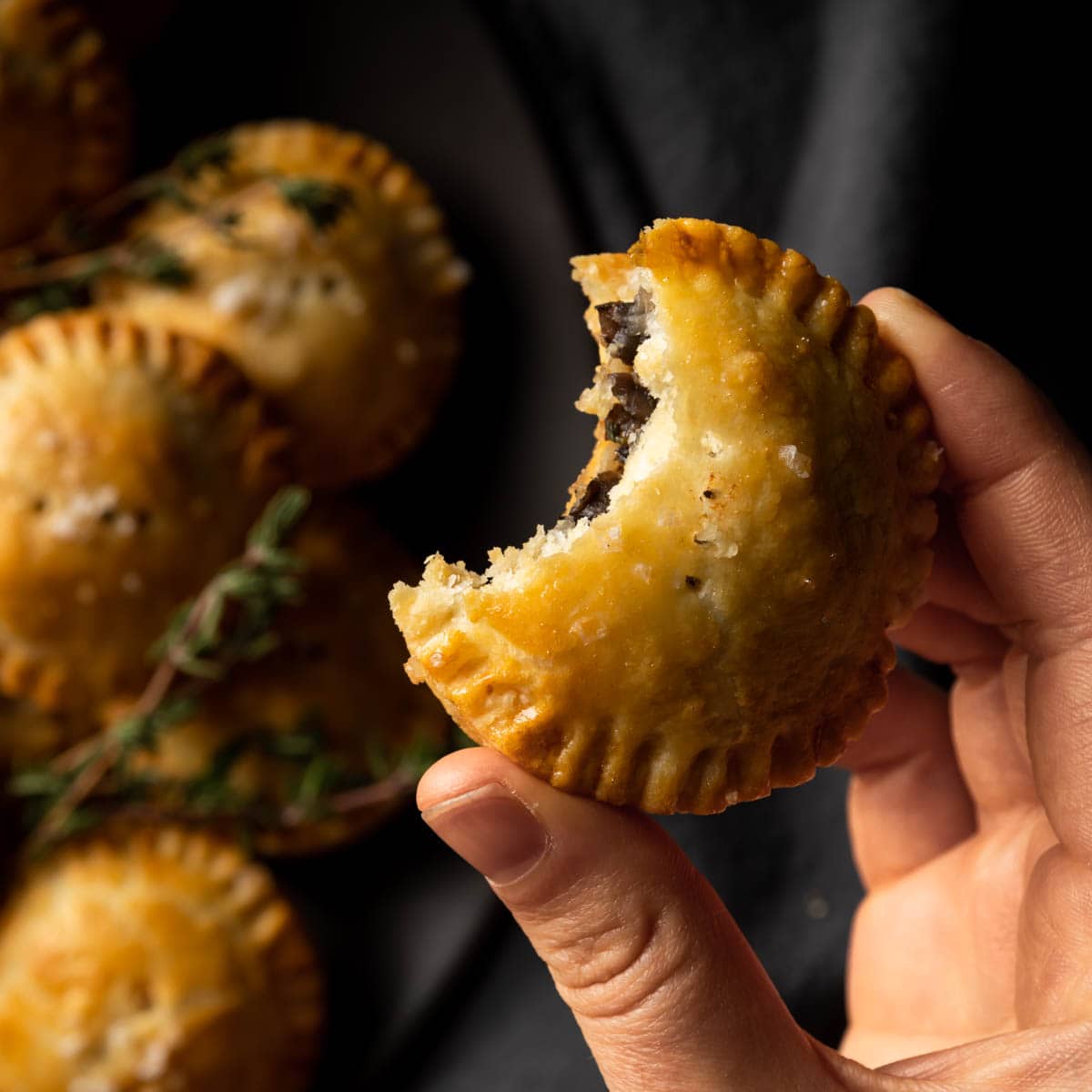 A close up of a hand holding a mini mushroom pie with a bite taken out of it.
