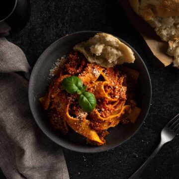 A flatlay photo of a big bowl of pasta with ragu alla bolognese topped with Parmesan and fresh basil leaves