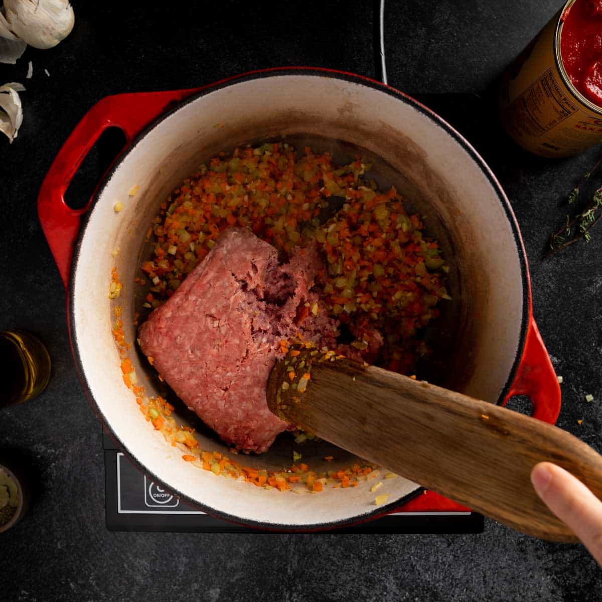 A pound of ground beef being added to a dutch oven with soffrito in it. 