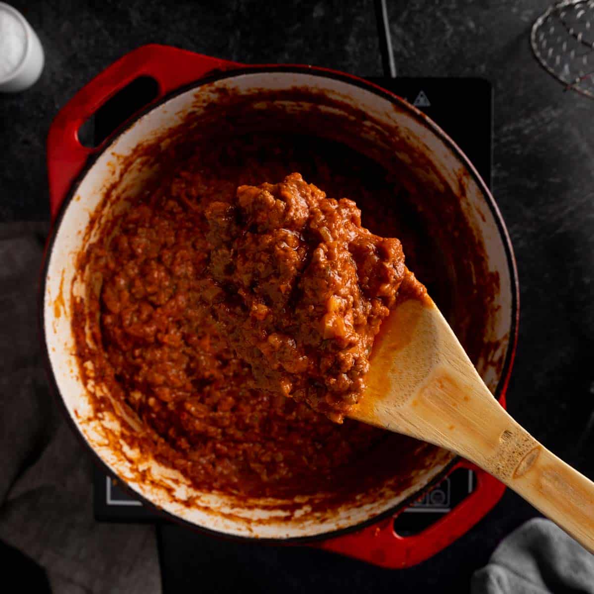 A wooden spoon holding up a big scoop of homemade Bolognese sauce