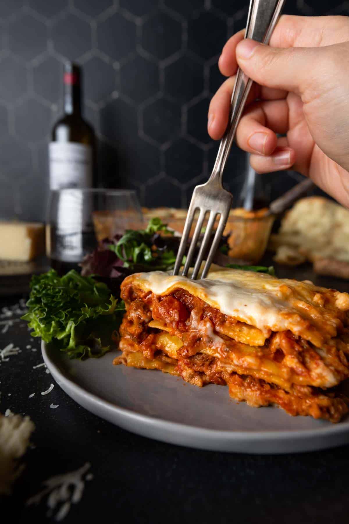 A fork going in for the first bite of a big slice of beef Bolognese lasagna. 