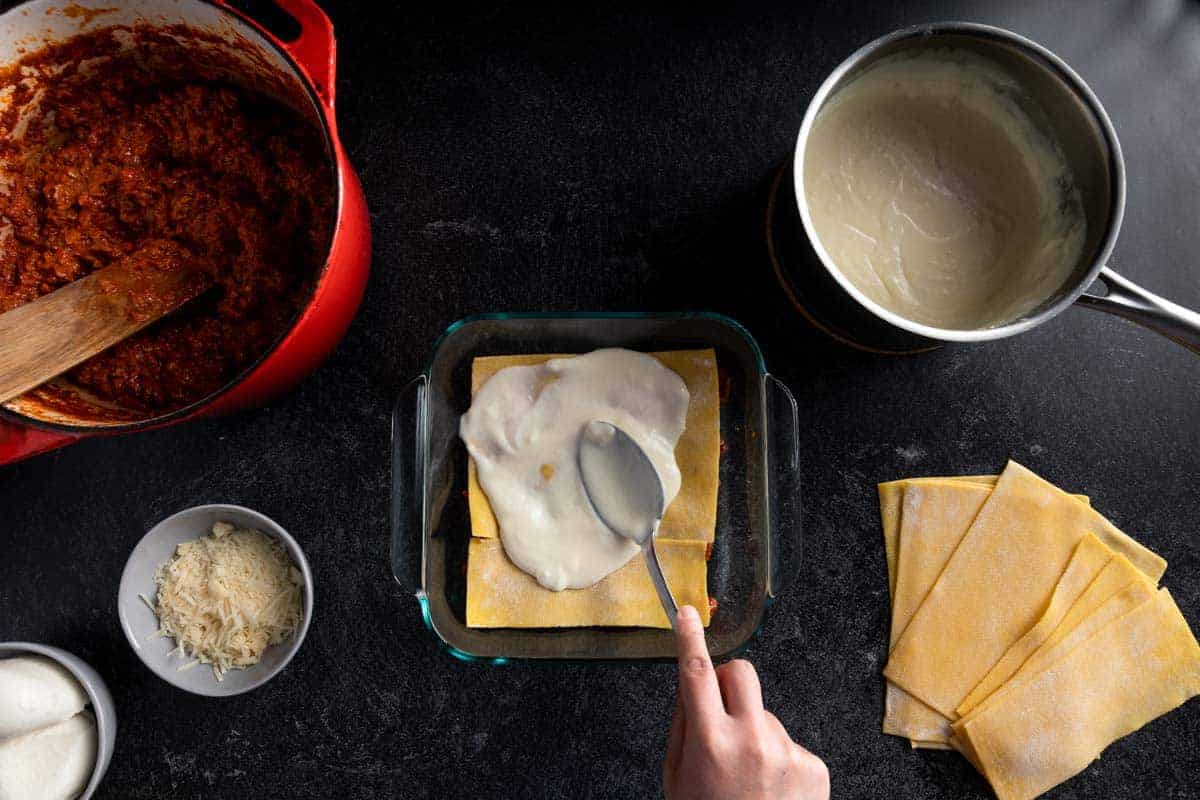 A spoon spreading Parmesan béchamel sauce over lasagna noodles