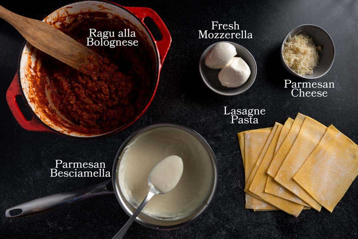 An image of all of the components needed for this authentic Italian lasagna recipe including Ragu all Bolognese, Parmesan besciamella, lasagna pasta sheets, and fresh mozzarella and shredded Parmesan cheeses.