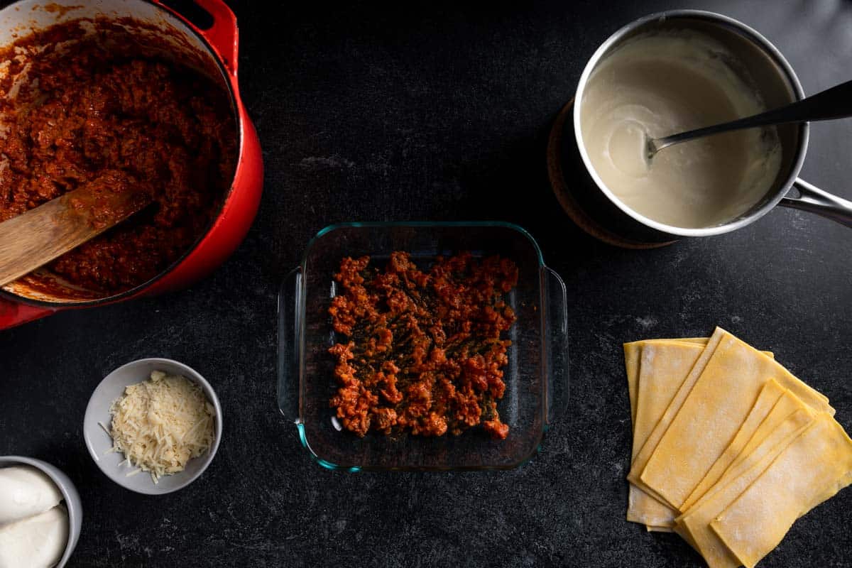 A small amount of beef Bolognese spread in the base of a square Pyrex baking dish