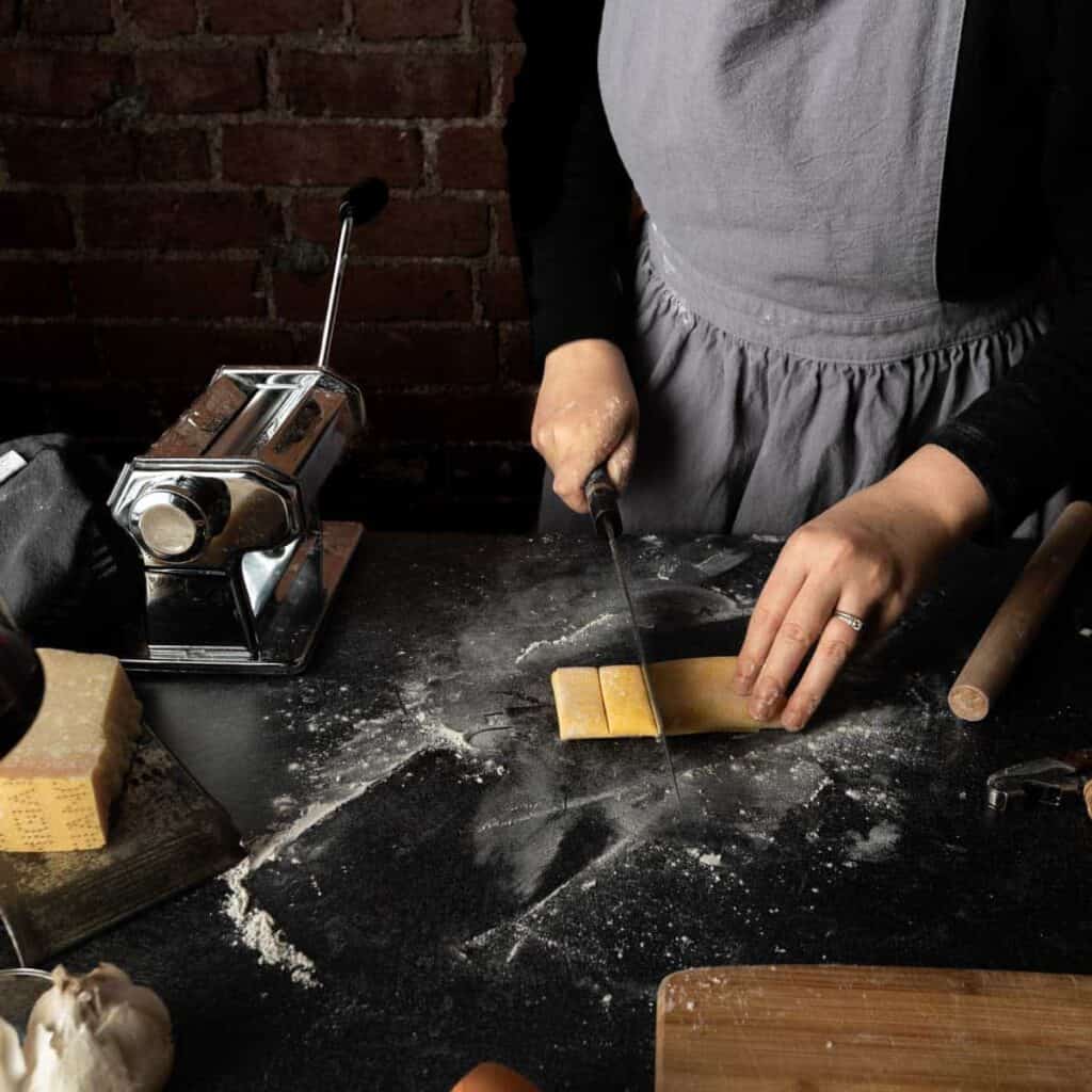 A woman cutting a folded tube of fresh pasta into wide noodles with a sharp chefs knife.