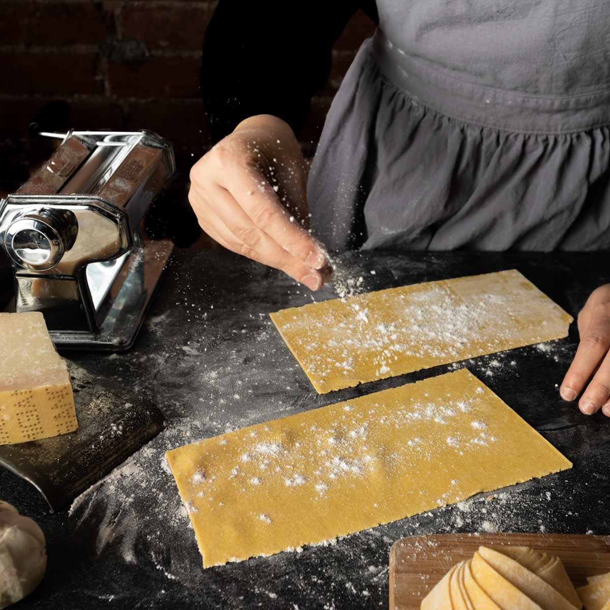 An aproned woman dusting flour on freshly made semolina lasagne sheets. 