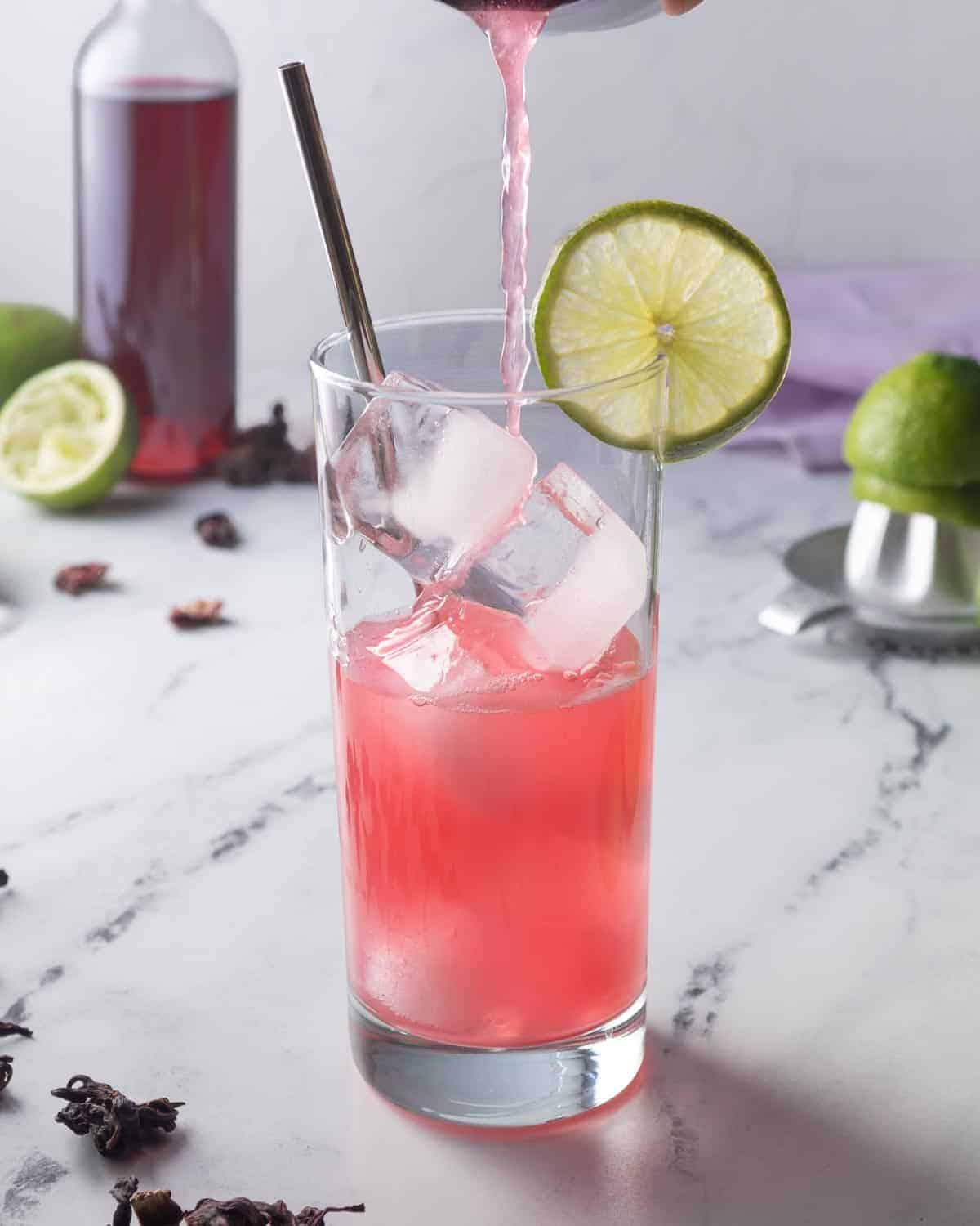 Hibiscus limeade being poured over ice cubes in a tall glass