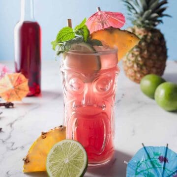 a close up image of hibiscus rum punch in a tiki glass