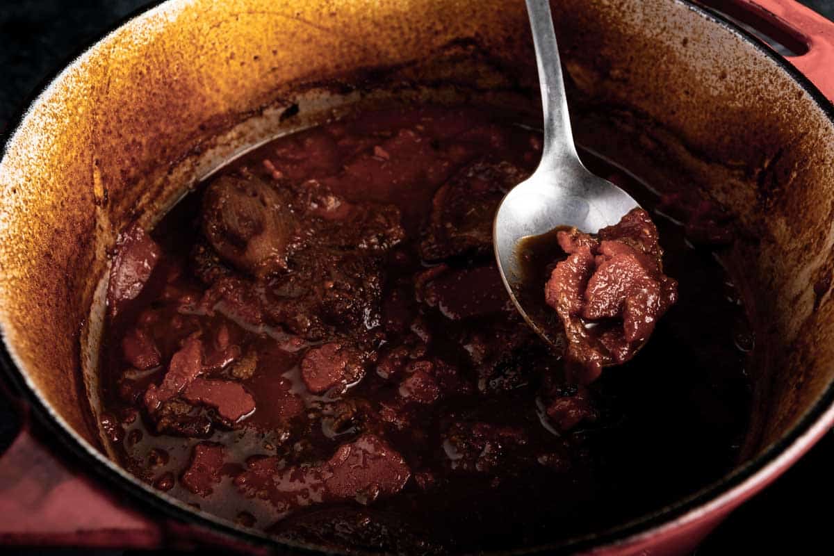 Using a spoon to scoop out the hardened layer of fat from the cooled short ribs in the dutch oven