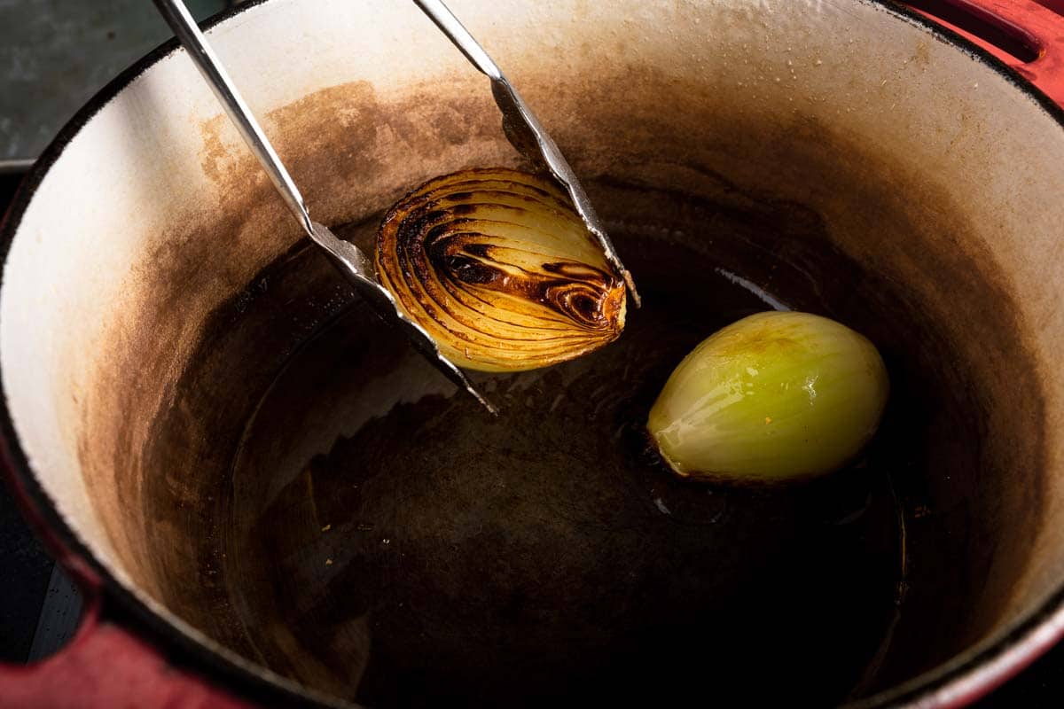 Tongs removing a seared onion fron a dutch oven