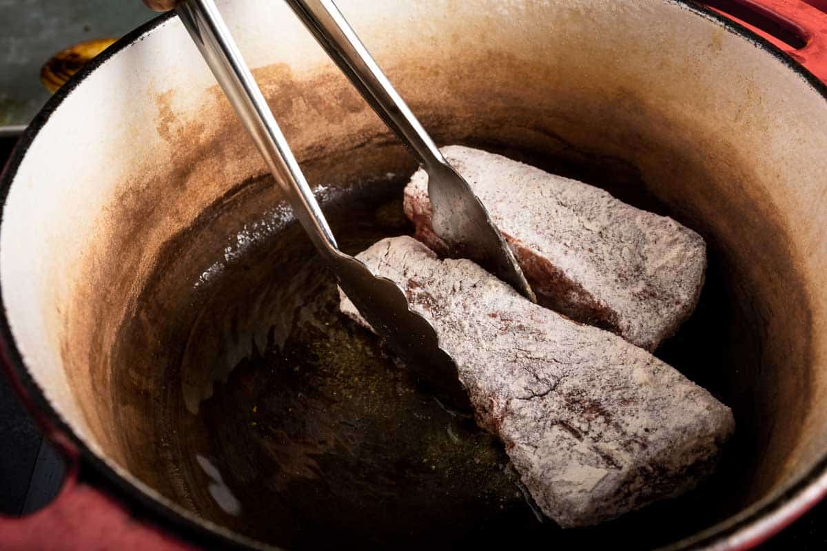 Floured short ribs being seared in a dutch oven