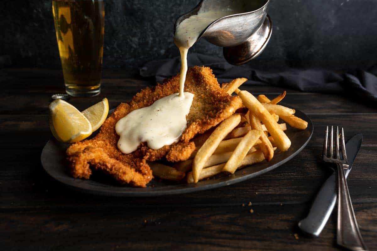 Pouring fondue sauce over a crispy fried pork schnitzel