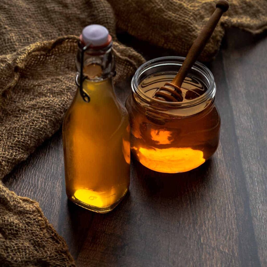 A bottle of honey syrup next to an open jar of honey with the dipper