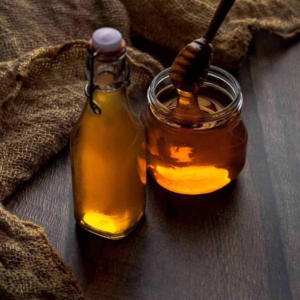 A bottle of honey syrup and jar of honey with dipper