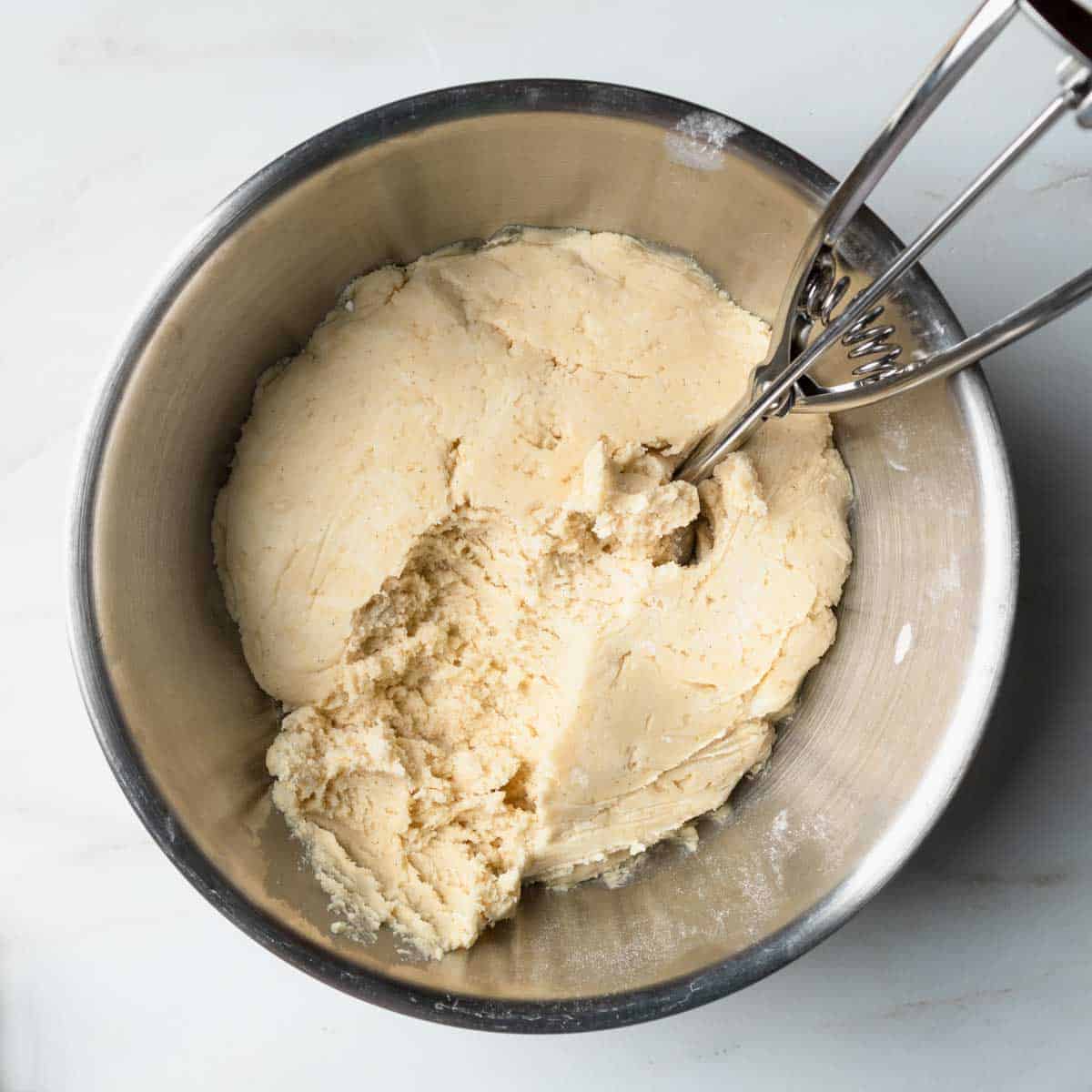A cookie scoop in a bowl of chilled vanilla cookie dough