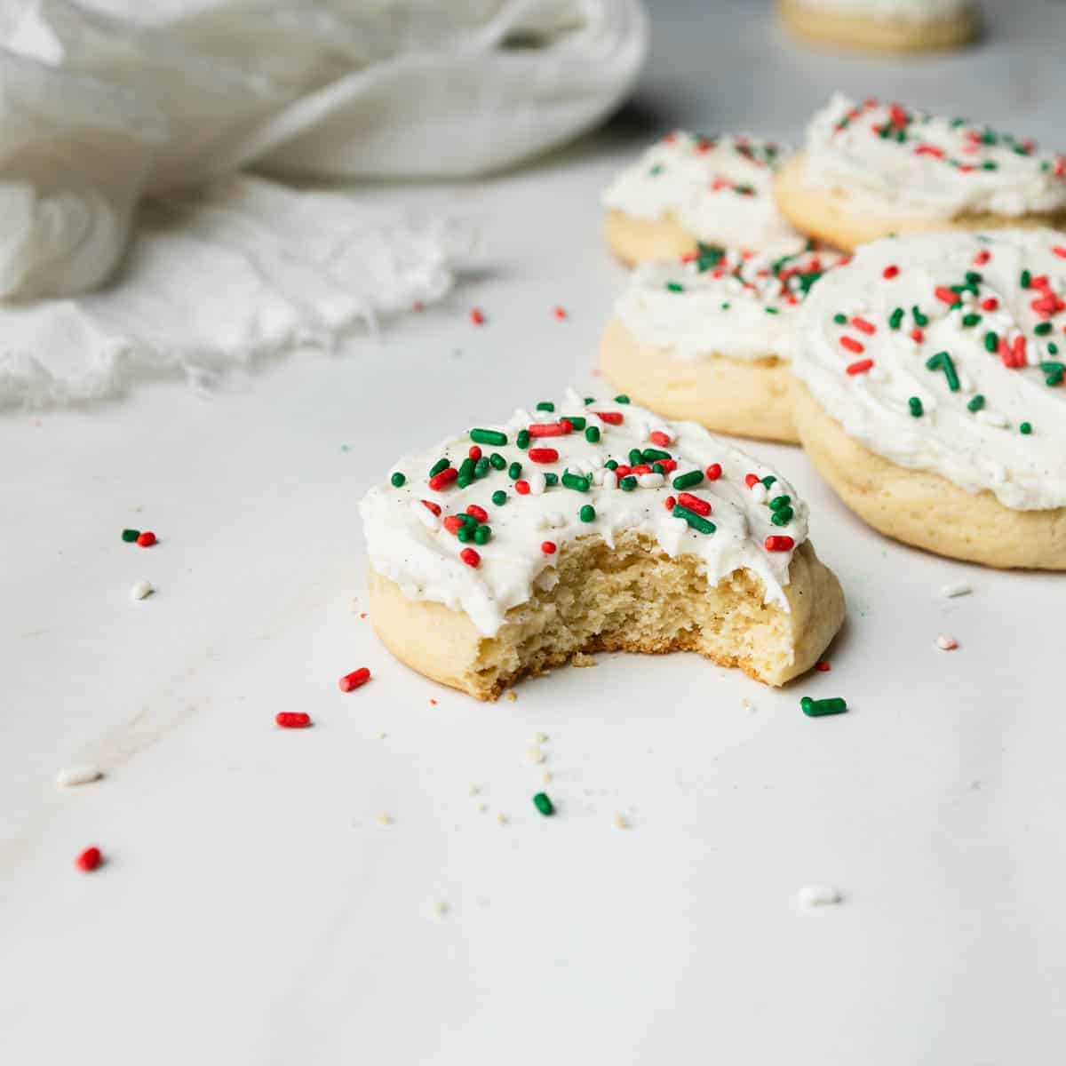 A bite taken out of a vanilla Christmas cookie topped with red and green sprinkles.