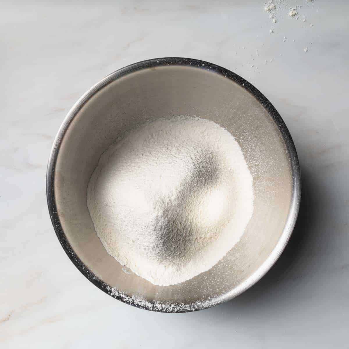 A metal bowl of sifted flour and other ingredients