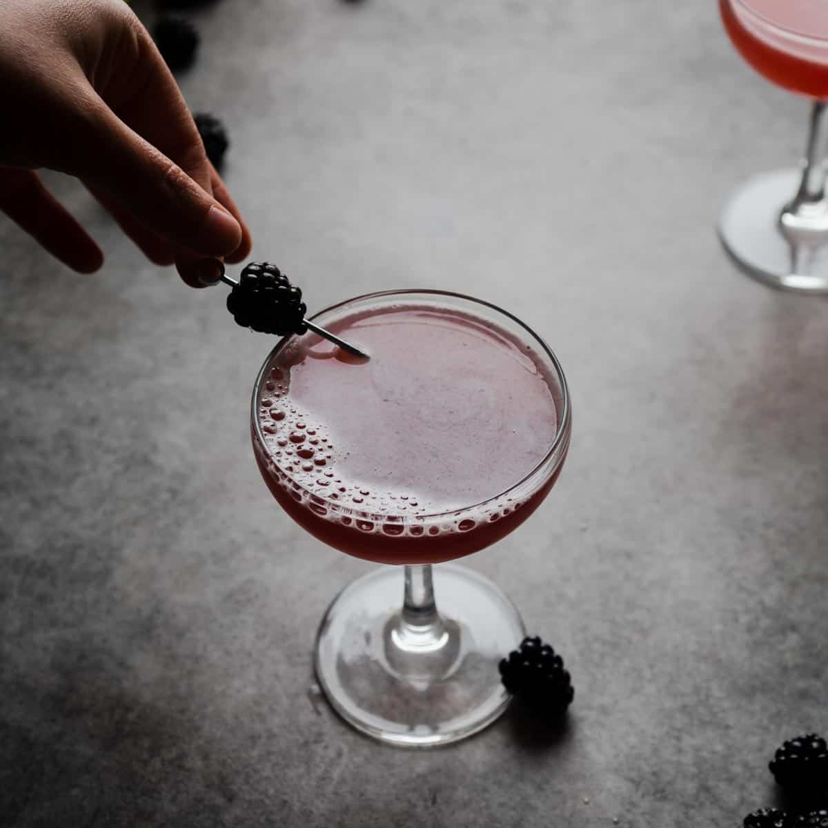 Placing a skewered blackberry garnish in the bees knees cocktail