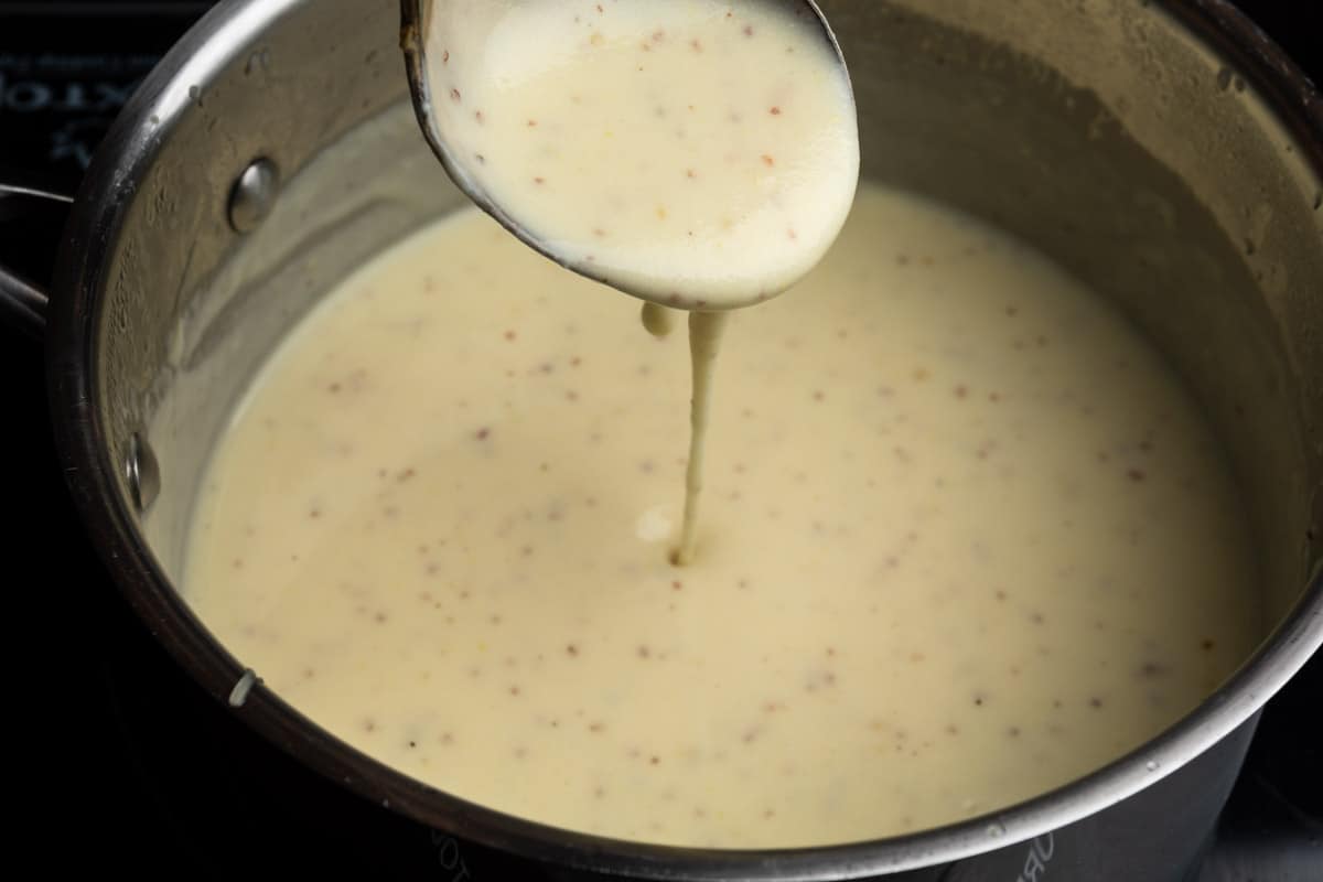 Cheesy mustard fondue sauce dripping from a ladle