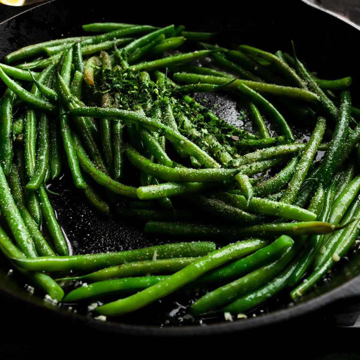 Seasoning the French green beans with salt, pepper, and fresh herbs