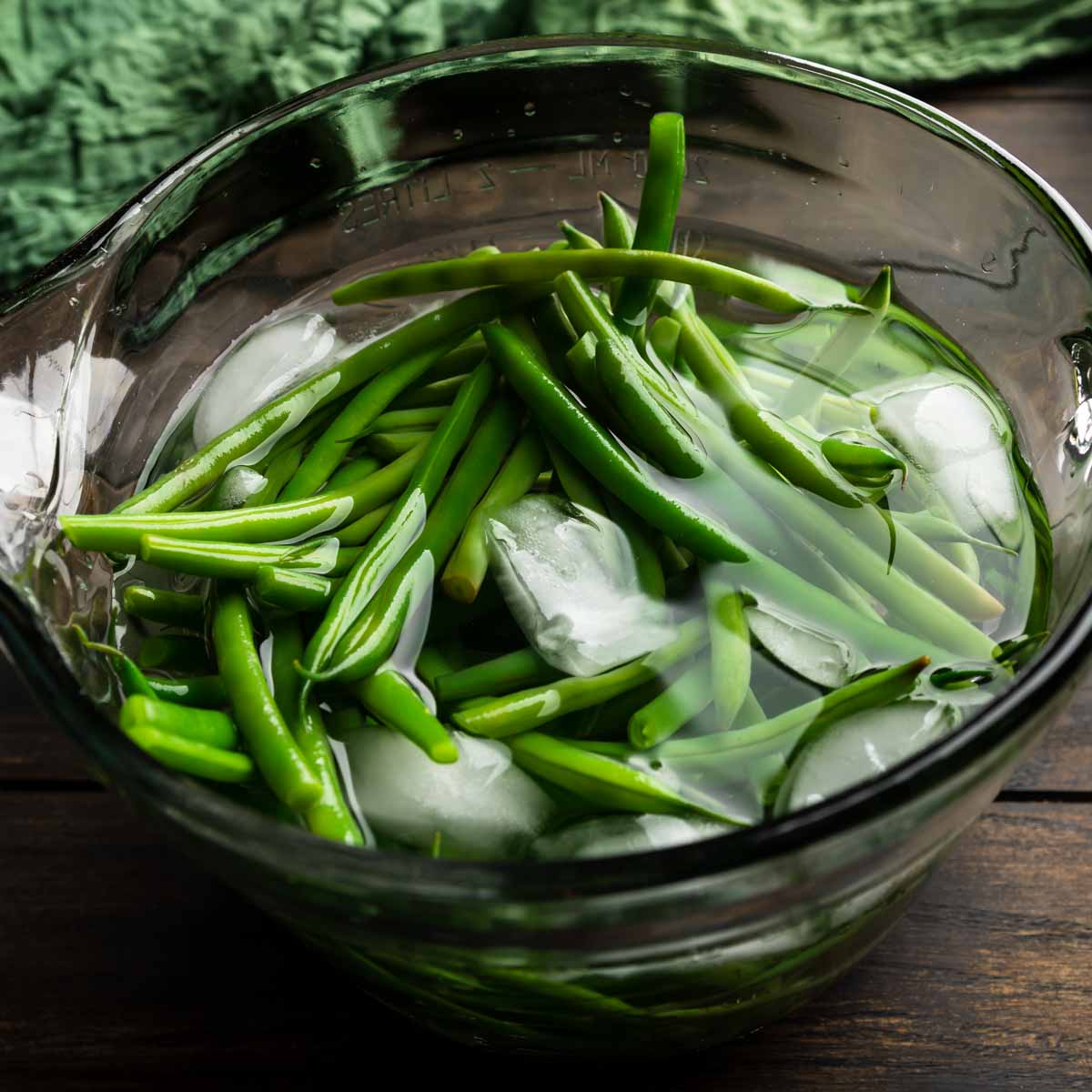A glass bowl full of steamed green beans in an ice water bath