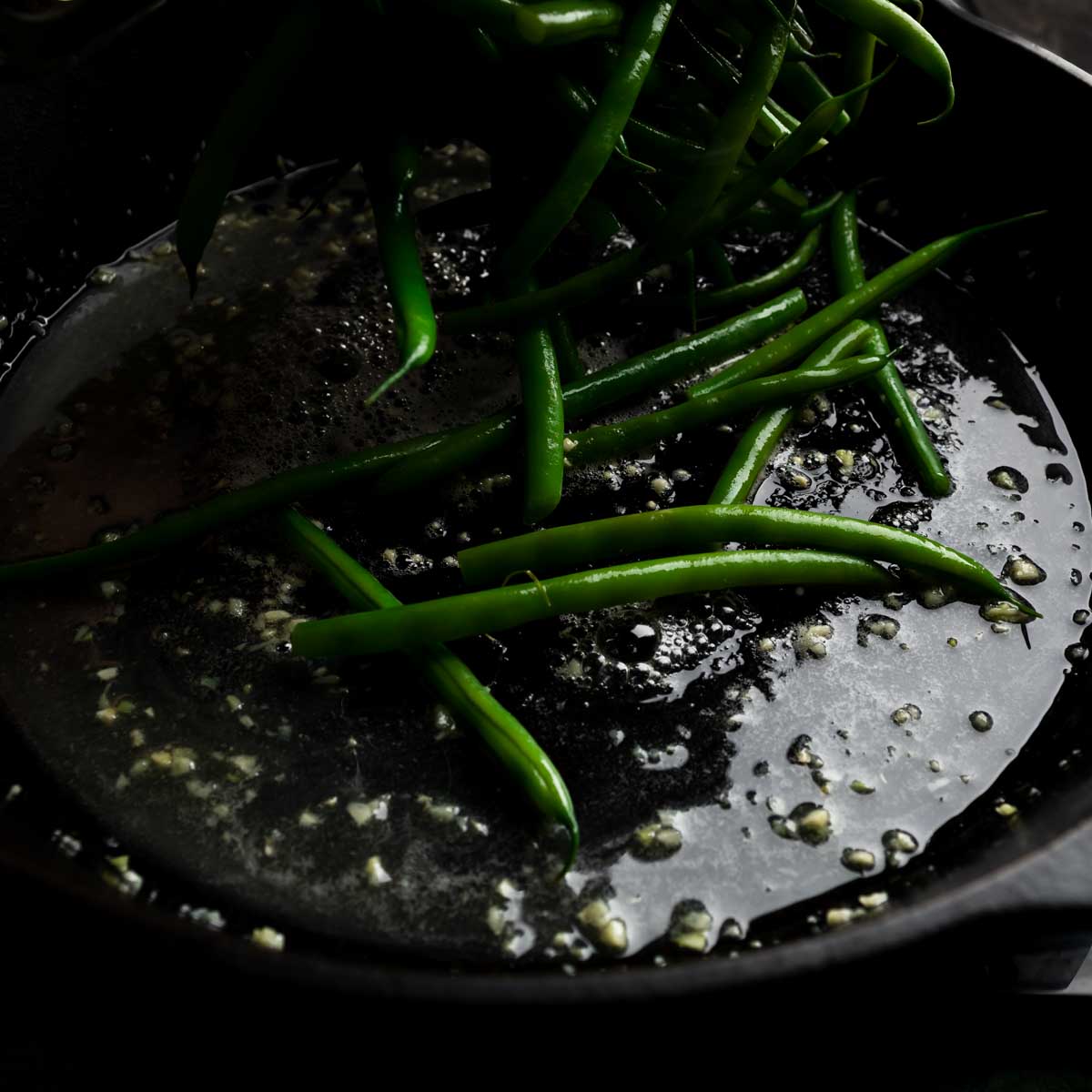 Adding green beans into the pan with the garlic butter