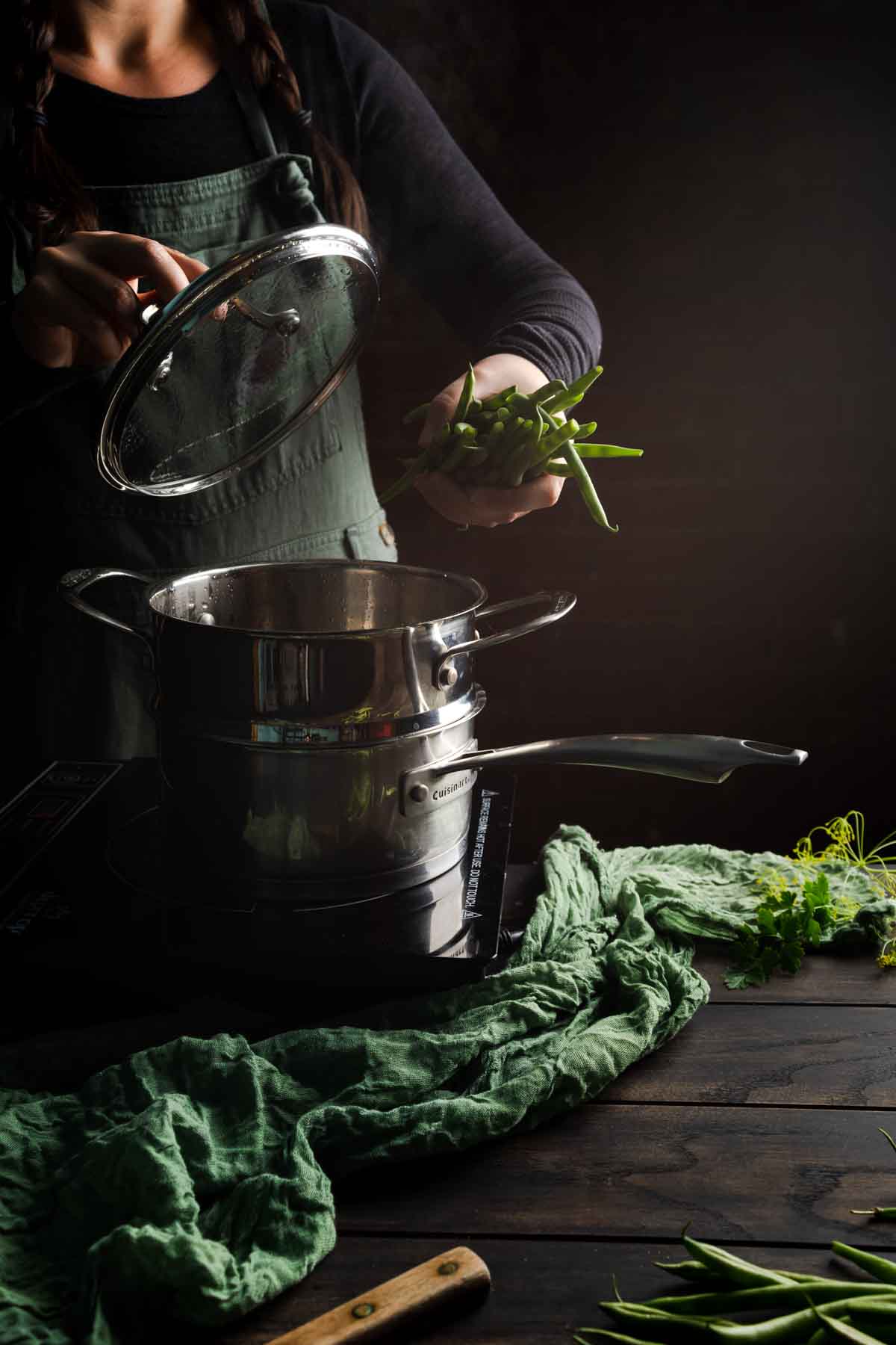 A woman dropping green beans into a steam basket