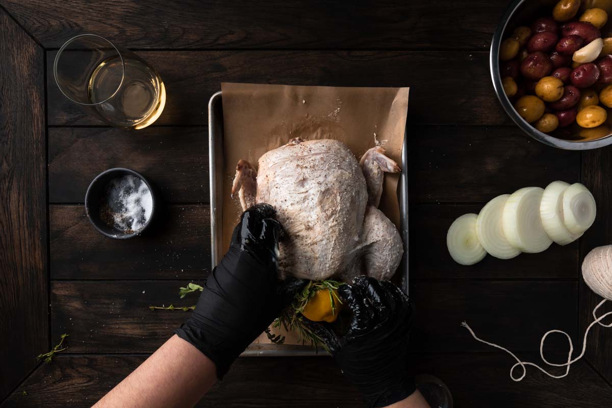 Stuffing the lemon and herbs into the cavity of a raw chicken.