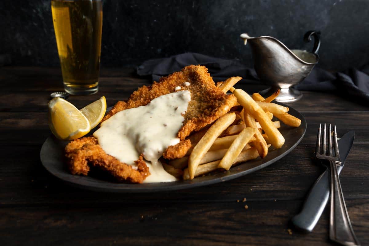 Crispy fried German schnitzel covered in cheese sauce on a plate with fries