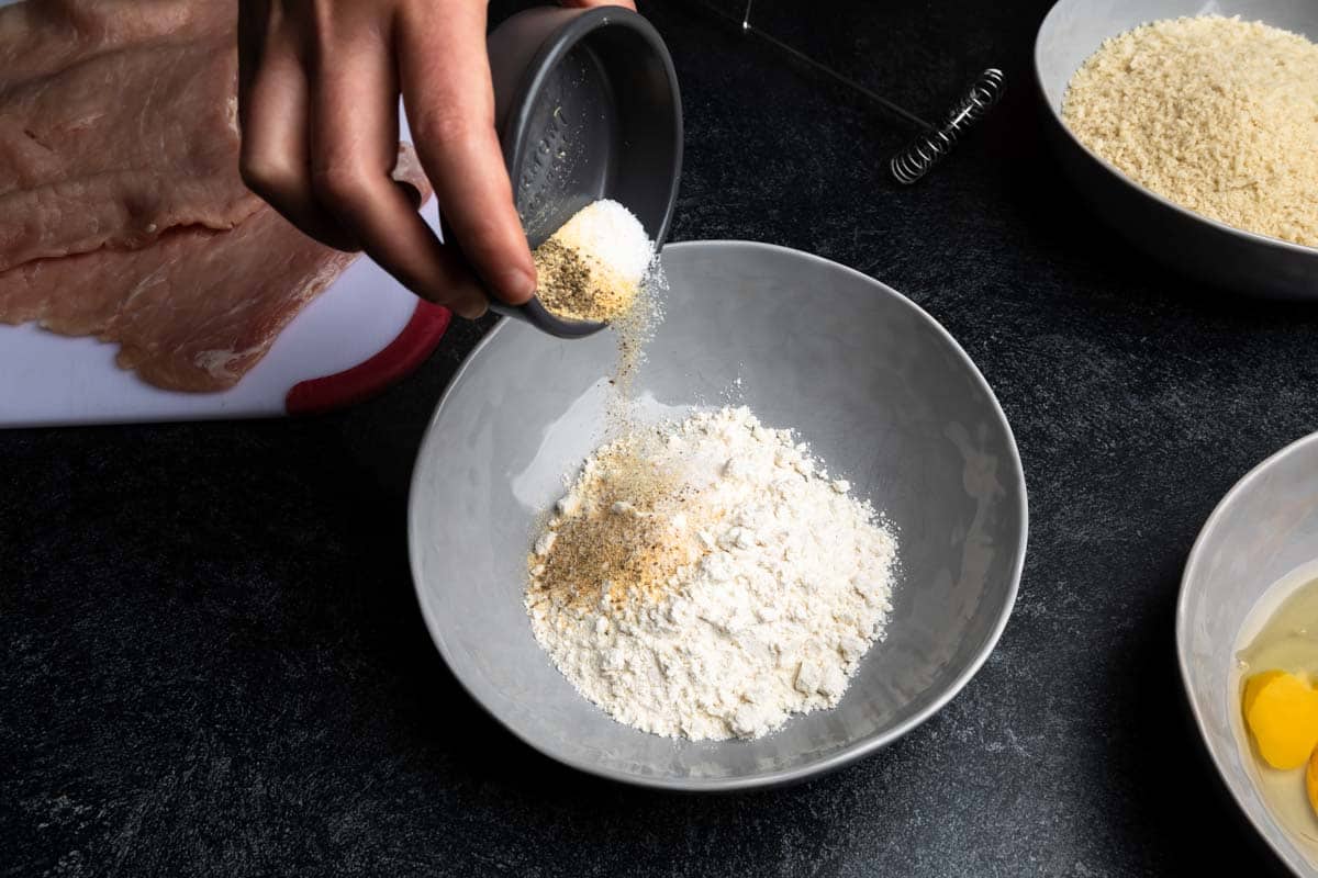 Sprinkling salt, pepper and garlic powder over a bowl of flour
