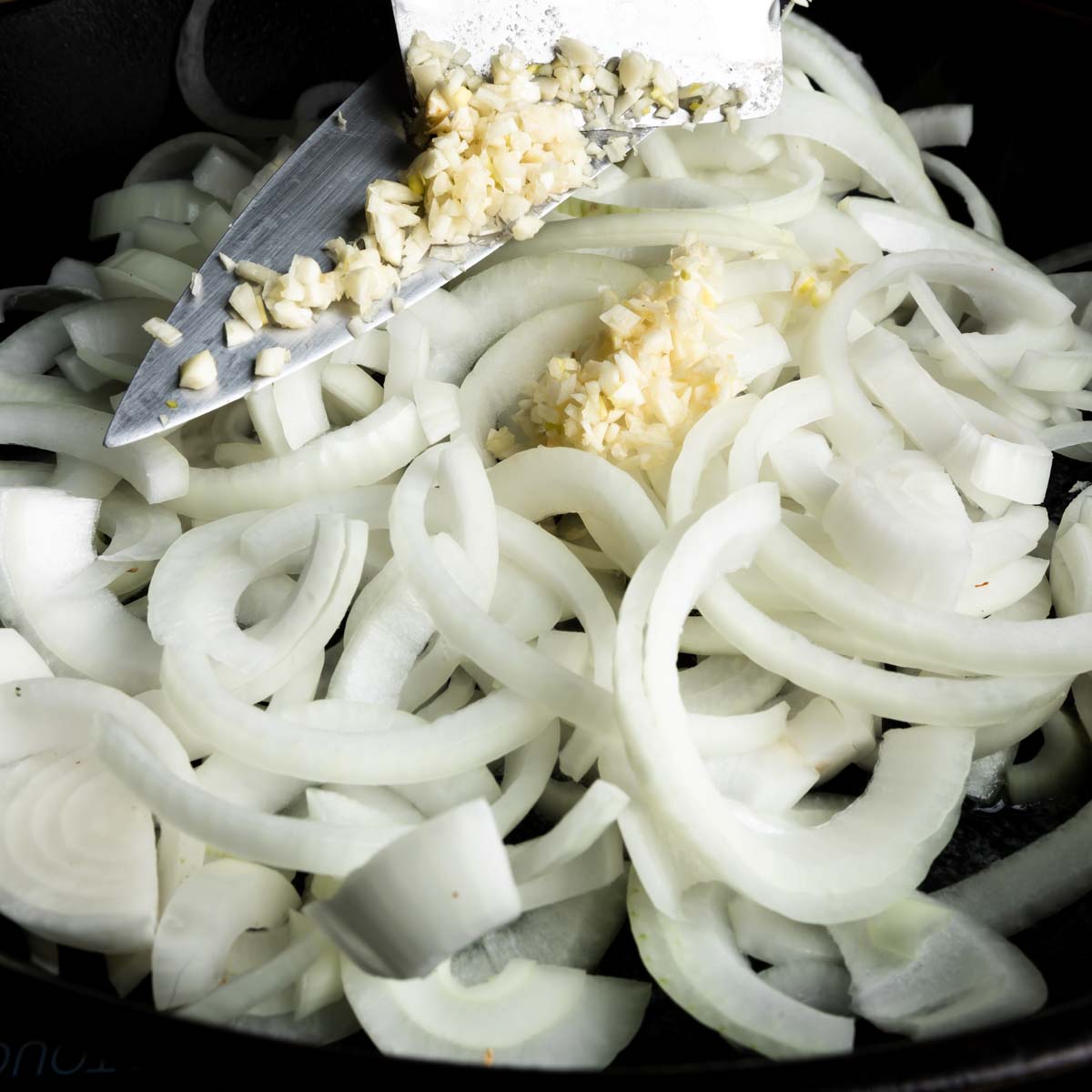 Adding sliced onions and minced garlic to a pan with butter