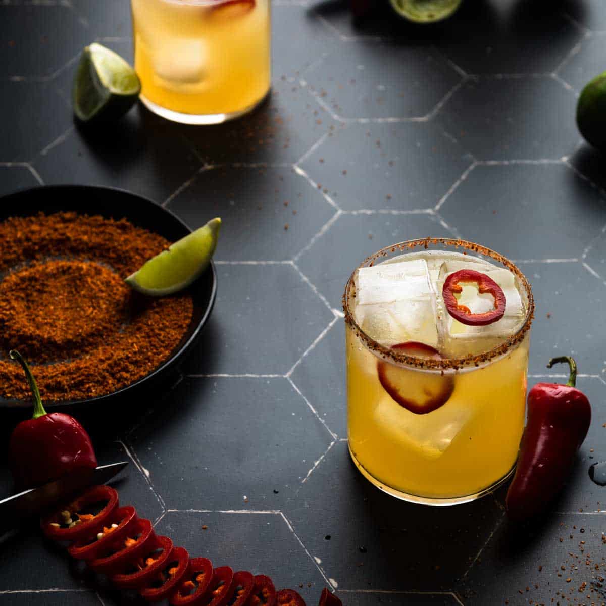 Spicy Mezcal margaritas next to a plate of tan and a sliced fresno chili