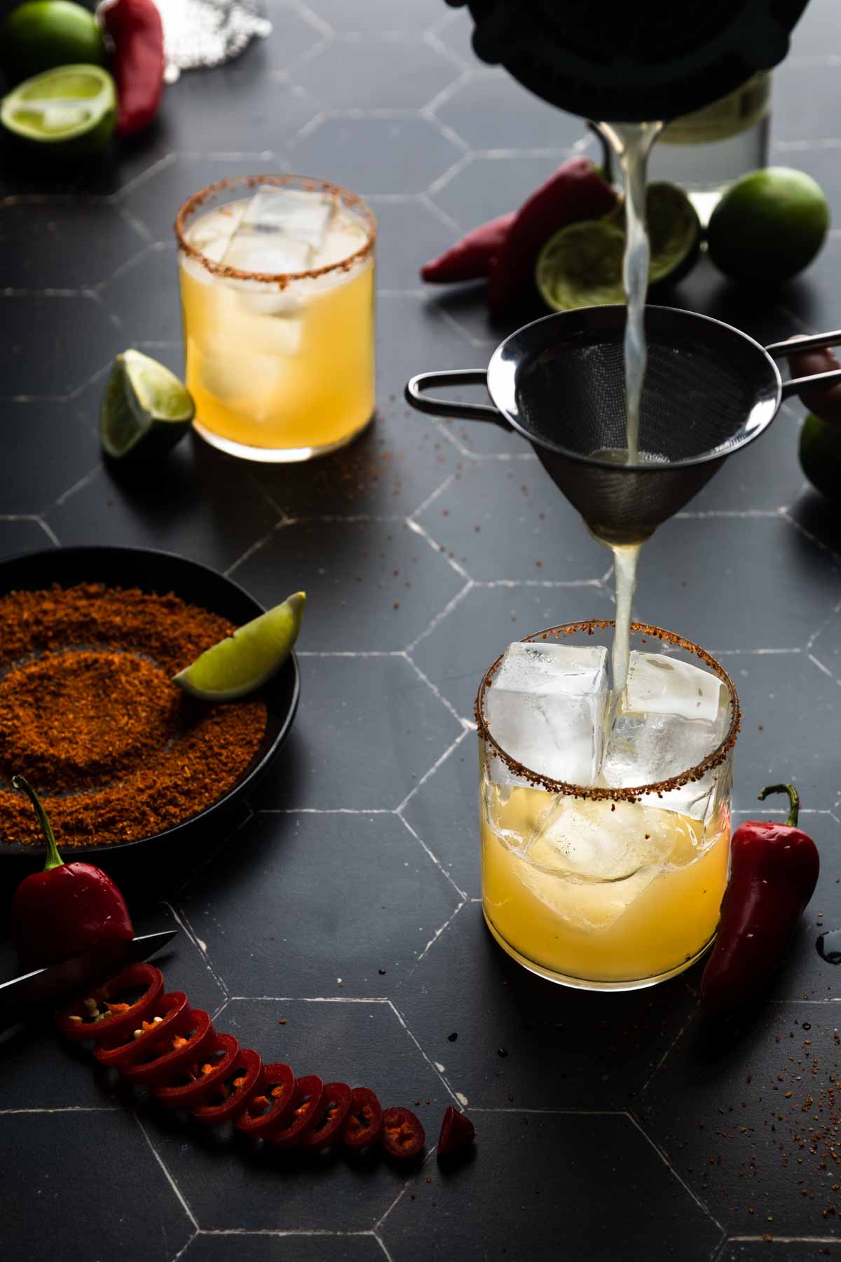 Pouring a margarita through a cocktail strainer into a glass with ice