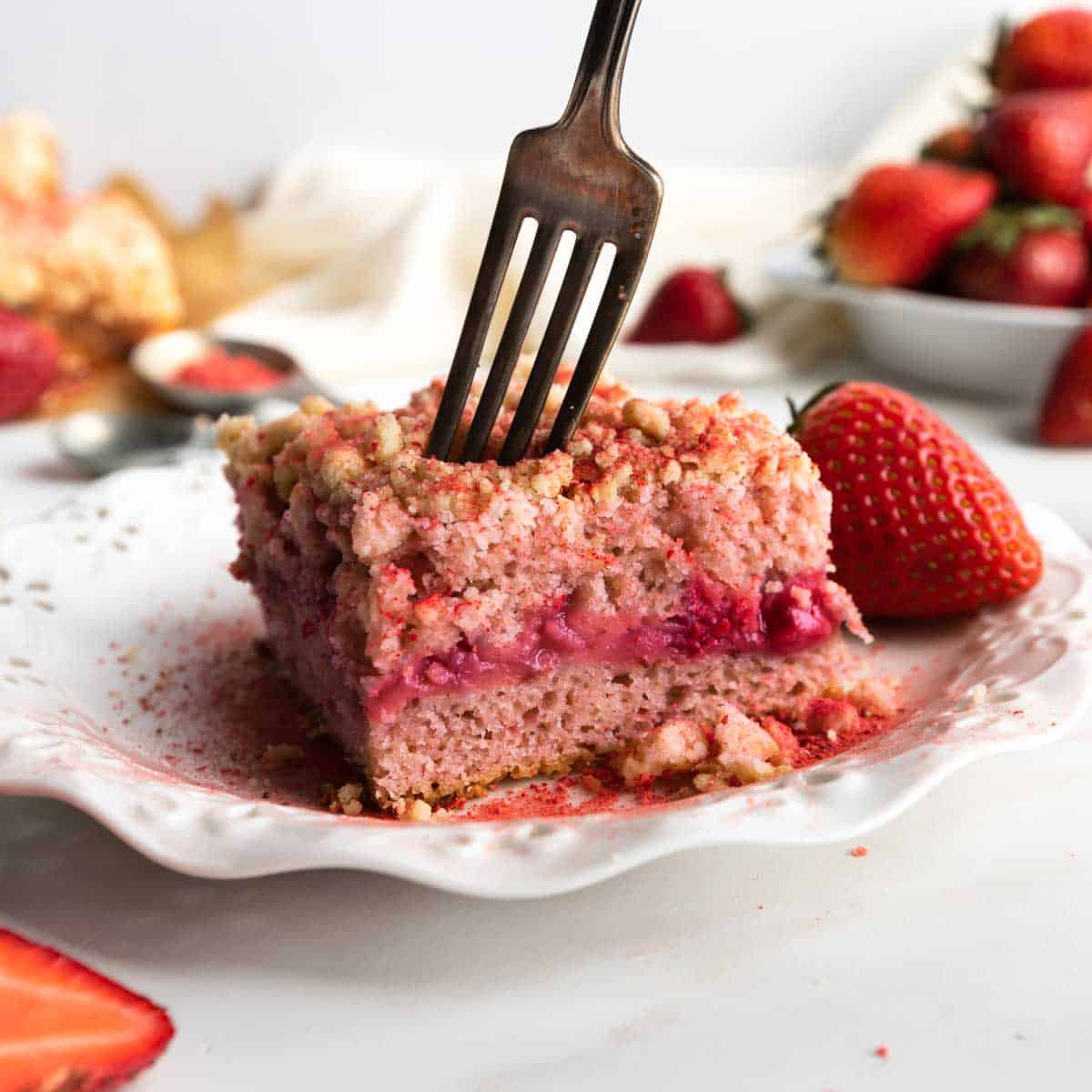 A fork sticking into a square slice of strawberry shortcake crumb cake