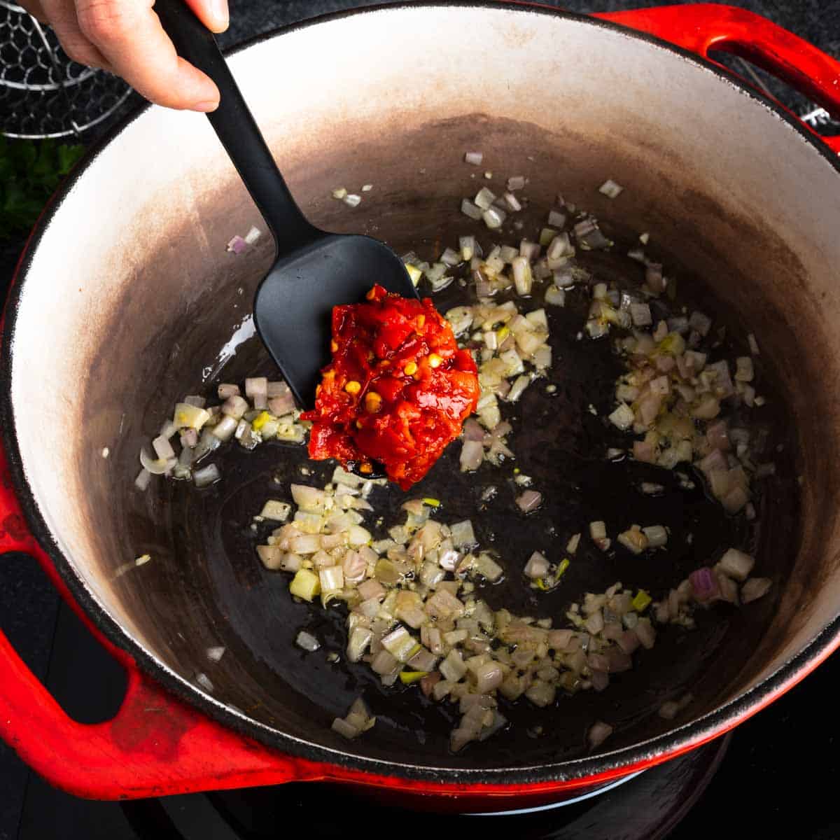 Adding Calabrian chili to a pot with shallots and oil