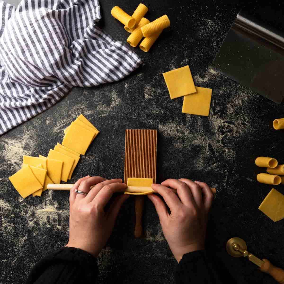 rolling a square of pasta dough around a wooden dowel over a gnocchi board