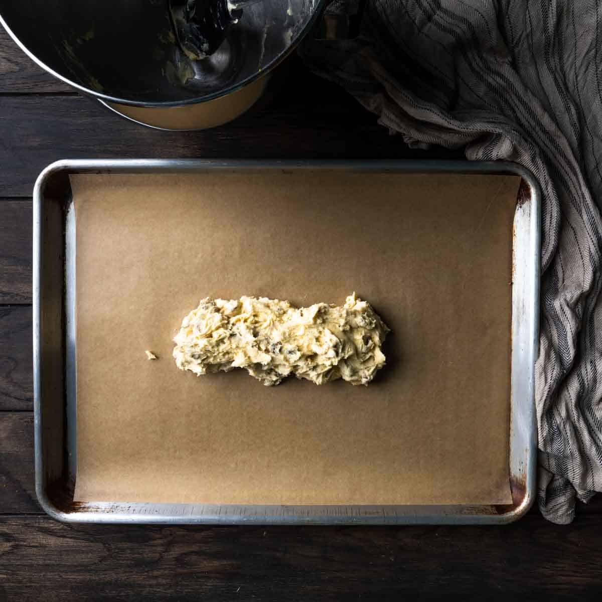 An irregular log of pistachio biscotti dough on a baking sheet
