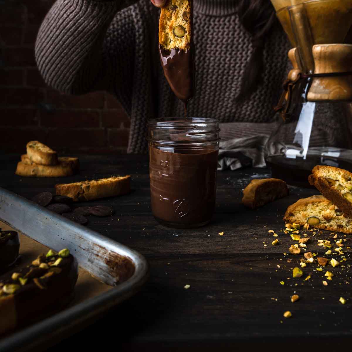 Dipping a pistachio biscotti into a jar of melted dark chocolate